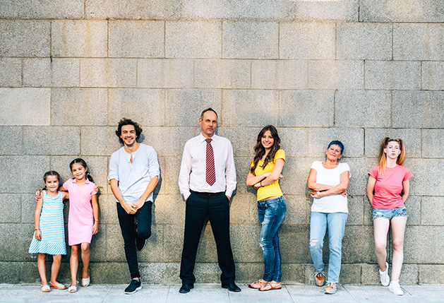 Seven people at different ages standing agains a wall.